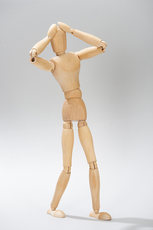 Wooden doll with hands by head on grey background