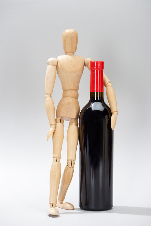 Wooden doll and bottle of red wine on grey background