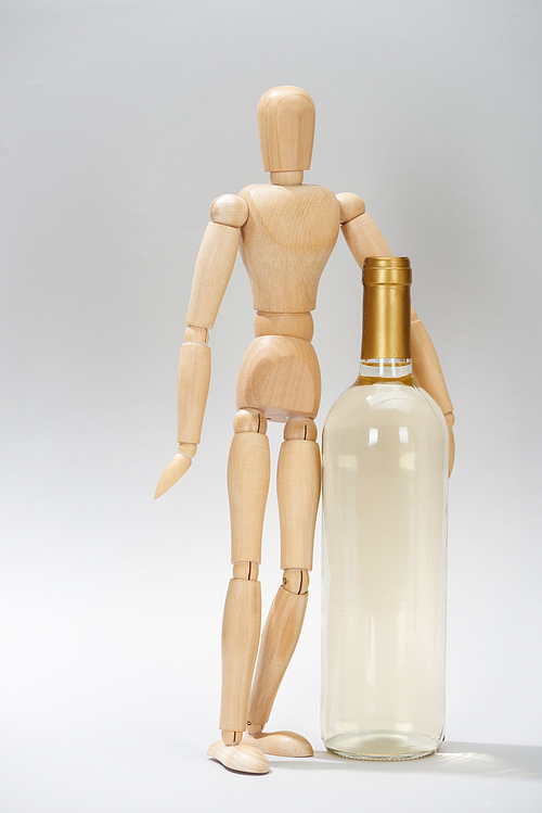Wooden puppet beside bottle of white wine on grey background