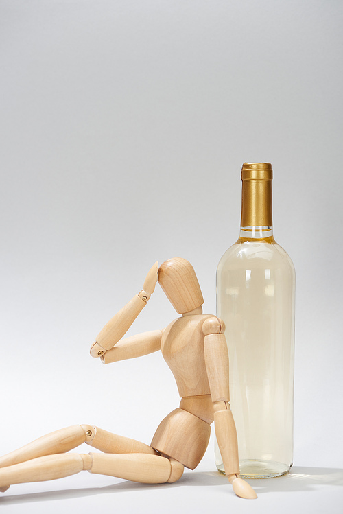 Wooden doll with hand by head beside wine bottle on grey background
