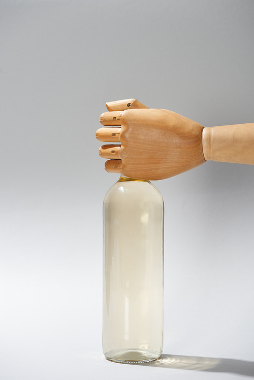 Wooden hand of dummy with bottle of wine on grey background