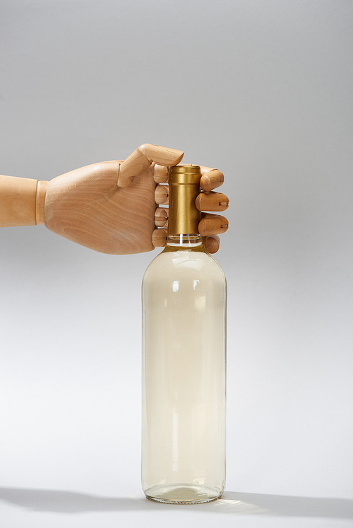 Hand of wooden doll with bottle of white wine on grey background