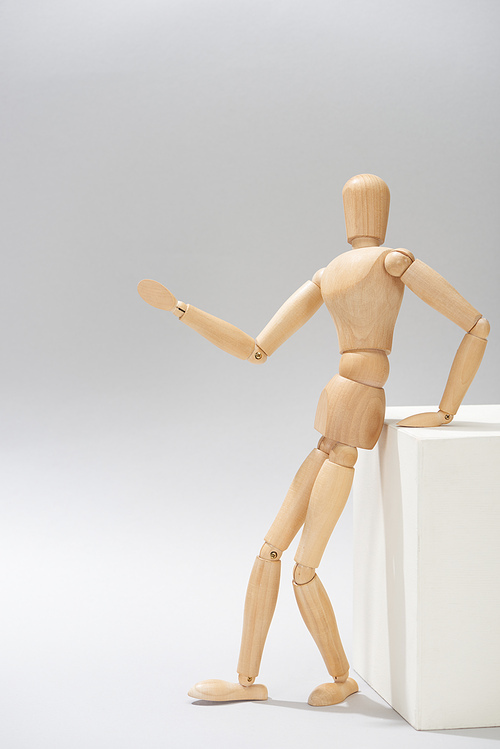 Wooden dummy by white stand pointing with hand on grey background
