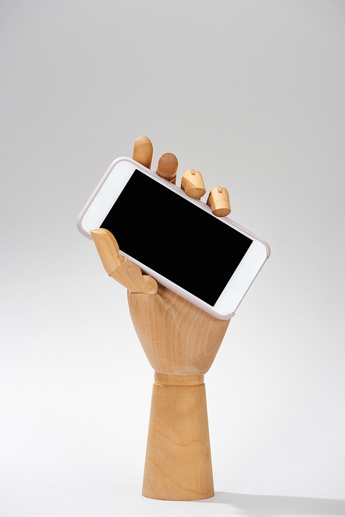 Wooden hand of doll with smartphone with blank screen on grey background