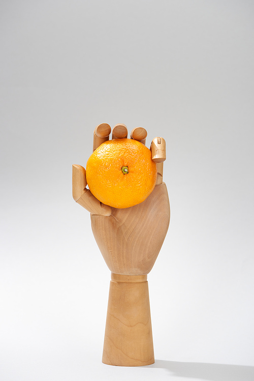 Wooden hand of doll with fresh mandarin on grey background