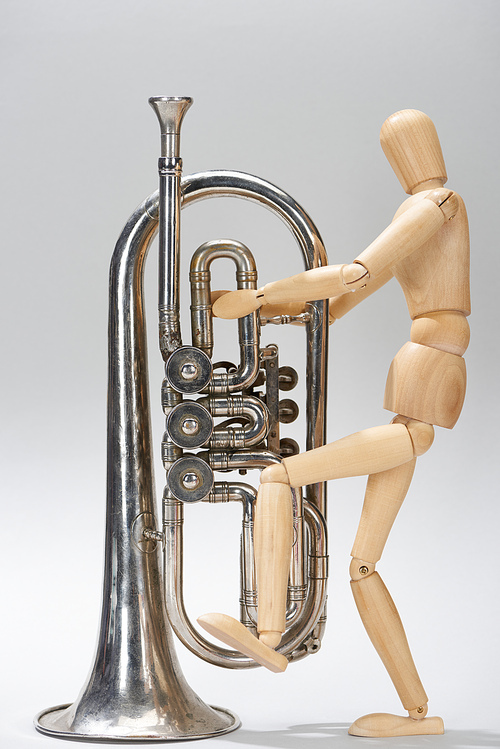 Wooden puppet with alto horn on grey background