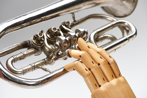 Close up view of wooden hand of doll with alto horn isolated on grey