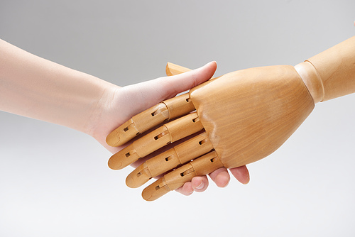 Cropped view of woman and wooden doll shaking hands isolated on grey