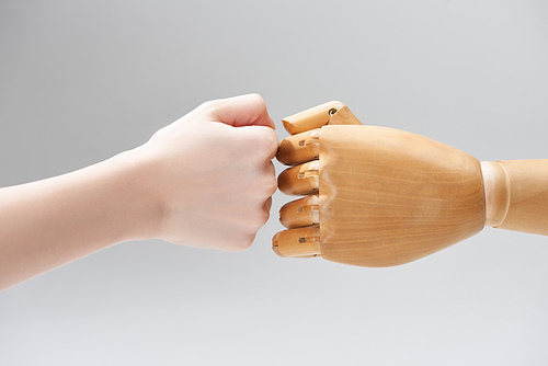 Cropped view of hands of woman and wooden doll making fist bump isolated on grey