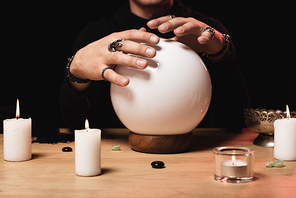 cropped view of esoteric holding hands above crystal ball near candles isolated on black