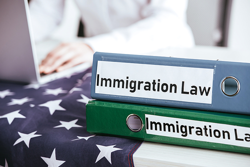 selective focus of folders with immigration law lettering with woman using laptop on background