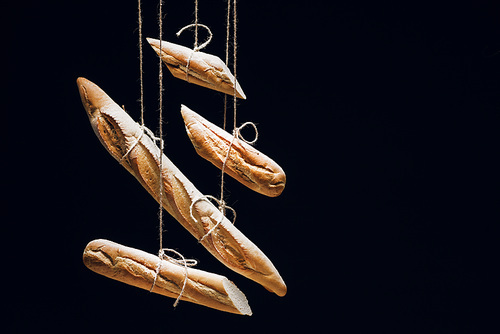 loaves of fresh baked baguettes on ropes isolated on black