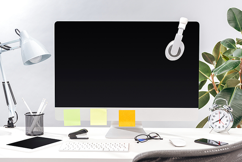 workplace with headphones and empty sticky notes on computer monitor, lamp and stationery on white table on grey background