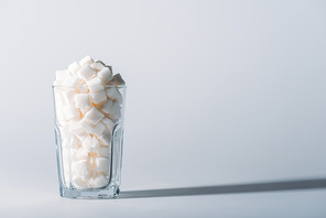 glass full of white sugar cubes on grey background with copy space