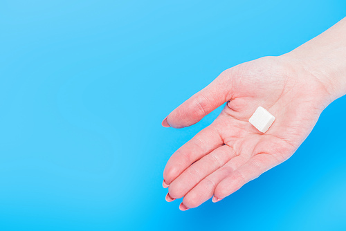 top view of female hand with white sugar cube on blue background