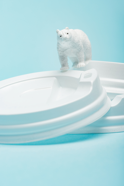 Toy polar bear on plastic coffee lids on blue background, animal welfare concept