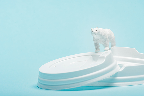 Toy polar bear on plastic coffee lids on blue background, ecological problem concept