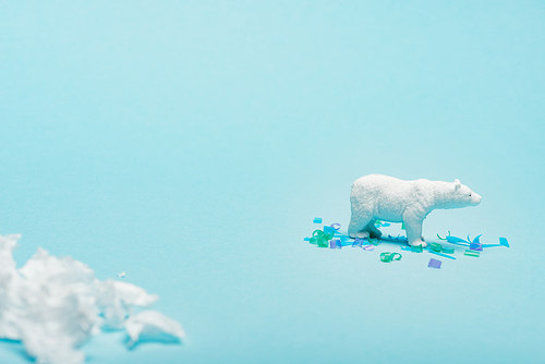 Selective focus of toy polar bear with polyethylene and plastic pieces on blue background, animal welfare concept