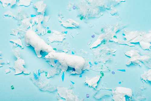 High angle view of toy polar bears with plastic pieces on blue background, environmental pollution concept