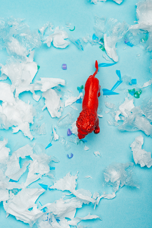 Top view of red toy lion on plastic garbage on blue background, animal welfare concept