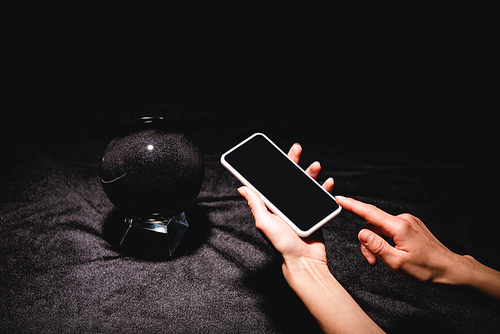 cropped view of astrologer holding smartphone near crystal ball on black velvet cloth