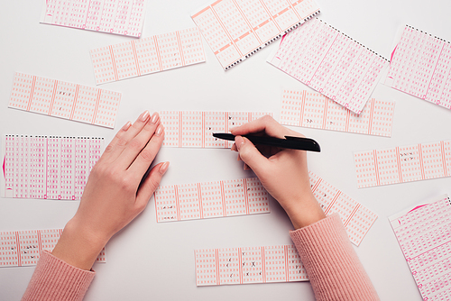 partial view of woman marking numbers on lottery tickets on white table
