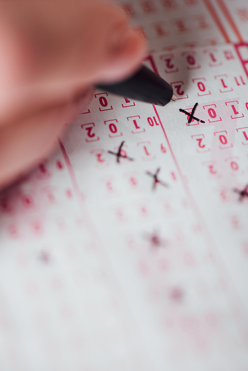 selective focus of hand of gambler marking numbers in lottery ticket