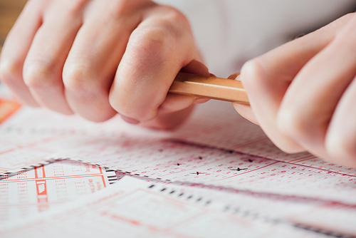 cropped view of upset gambler braking pencil near lottery tickets