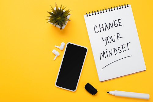 notebook with change your mindset inscription near smartphone, wireless headphones, potted flower and felt-tip pen on yellow table