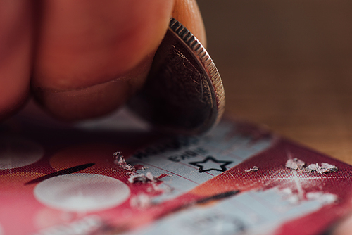 close up view of silver coin in hand of gambler scratching lottery ticket