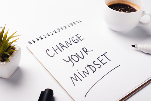 notebook with change young mindset inscription, felt-tip pen, coffee cup and potted plant on white surface