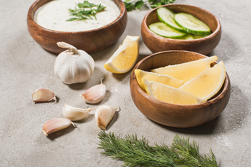 Selective focus of lemon, cucumber with garlic and tzatziki sauce on stone surface