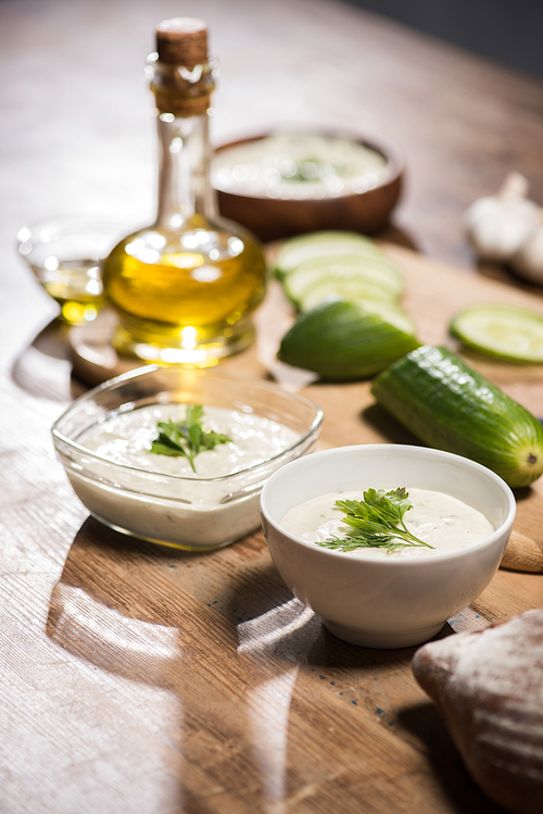 Tzatziki sauce in bowls with ingredients and olive oil on wooden table