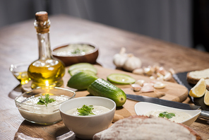Delicious tzatziki sauce with ingredients and olive oil on wooden kitchen table