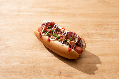 delicious hot dog with red onion, bacon and Dijon mustard on wooden table