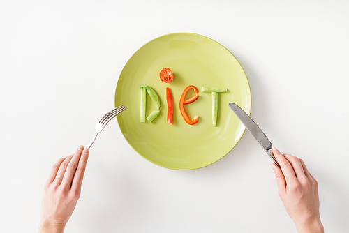 Top view of woman with cutlery near word diet from vegetable slices on plate on white background