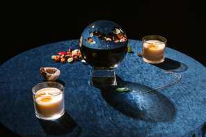 Crystal ball near candles and fortune telling stones on dark blue velour cloth isolated on black