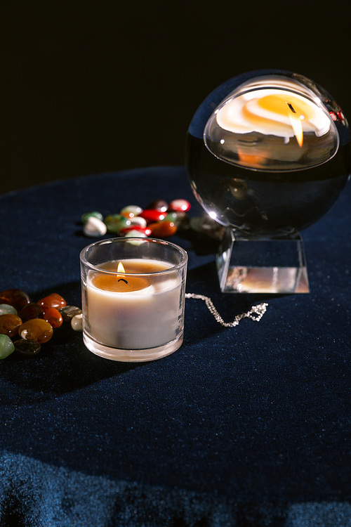 Selective focus of crystal ball, candle, fortune telling stones on dark blue velour fabric isolated on black
