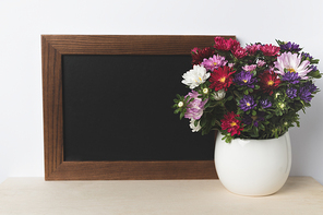close-up view of blank board and beautiful blooming flowers in vase on table