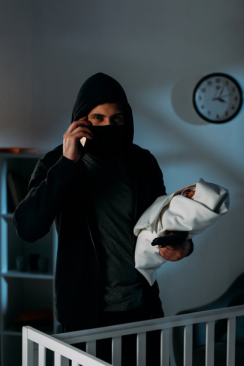 Kidnapper with gun holding infant child and talking on smartphone