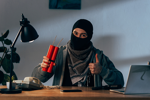 Terrorist in mask holding dynamite and showing thumb up in room