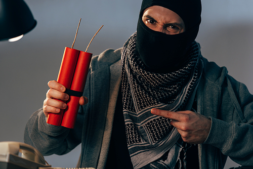 Aggressive terrorist pointing with finger at dynamite and 