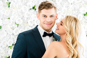 happy beautiful bride hugging handsome groom on white floral background