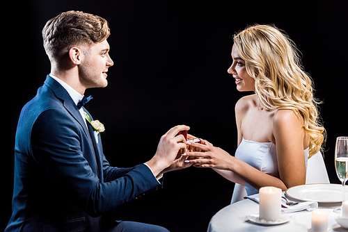 handsome young man making marriage proposal to happy young woman isolated on black