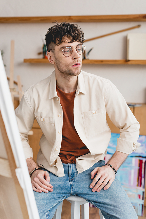 selective focus of serious artist in eyeglasses looking away