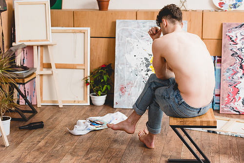 exhausted half-naked artist sitting on chair in painting studio