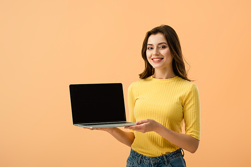 Cheerful brunette girl showing laptop with blank screen isolated on orange