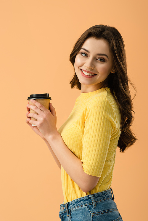 Laughing attractive girl holding paper cup of coffee and  isolated on orange