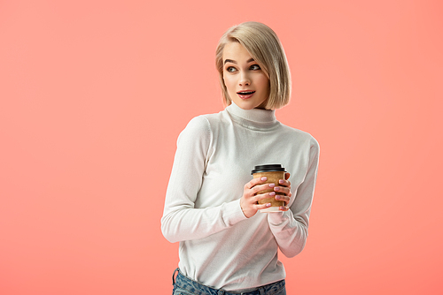 shocked blonde girl holding paper cup with drink isolated on pink