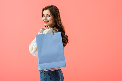 smiling and attractive young woman holding shopping bag isolated on pink